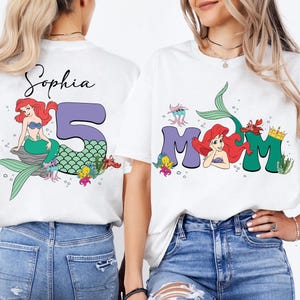 May include: White t-shirts with mermaid-themed graphics. One shirt features the name "Sophia" with a mermaid and the number "5". The other shirt says "MOM" with a mermaid and crown.