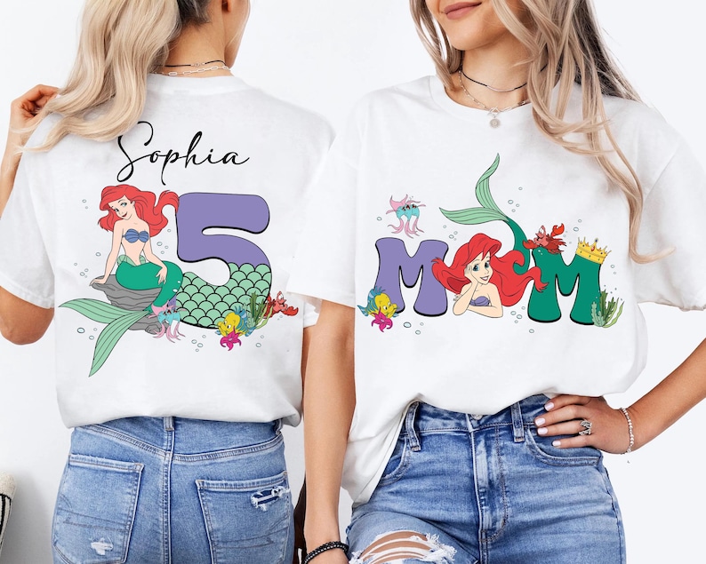 May include: White t-shirts with mermaid-themed graphics. One shirt features the name "Sophia" with a mermaid and the number "5". The other shirt says "MOM" with a mermaid and crown.