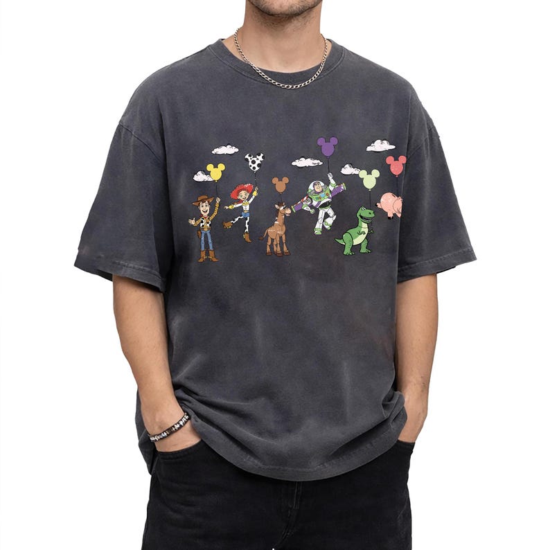 Op de afbeelding: Donkergrijs T-shirt met een kleurrijke afbeelding van Toy Story-personages die ballonnen vasthouden. Het ontwerp bevat Woody, Jessie, Buzz Lightyear en Rex. Het shirt heeft een vintage wassing en een relaxte pasvorm.