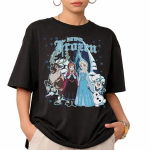 May include: Black t-shirt featuring characters from the movie Frozen, including Elsa, Anna, Olaf, and Sven. The shirt has the words "Let It Go Frozen" in blue. Snowflakes and a snowy mountain scene are also depicted.