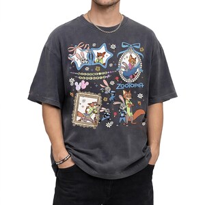 May include: A charcoal gray short-sleeve t-shirt featuring a Zootopia graphic print. The design includes illustrations of Judy Hopps and Nick Wilde within star-shaped and oval frames, with the text Welcome to Zootopia and Zootopia printed.