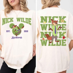 May include: An off-white t-shirt featuring Nick Wilde from Zootopia. The front displays the text NICK WILDE, EST. 2016, and ZOOTOPIA with a green Mickey-shaped icon. The back shows Nick Wilde with the text NICK WILDE in large green letters.