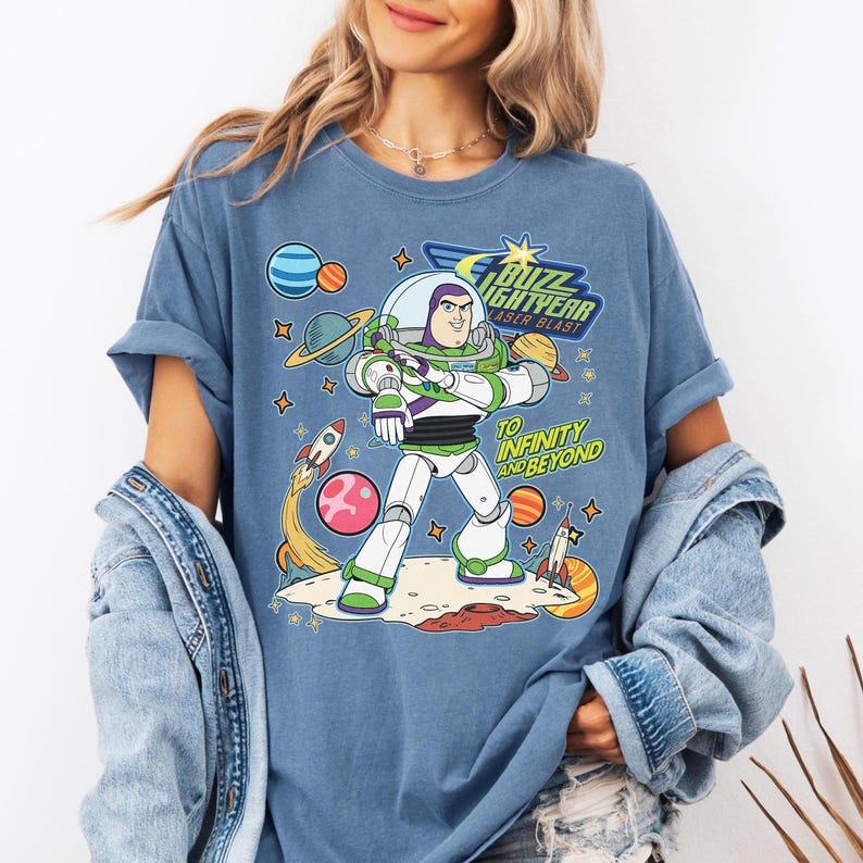 May include: Blue t-shirt featuring Buzz Lightyear from Toy Story. The graphic includes the text "Buzz Lightyear Laser Blast" and "To Infinity and Beyond" with planets, rockets, and stars. The shirt has rolled-up sleeves.