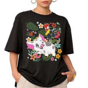 Puede incluir: Camiseta negra con un dise&ntilde;o de cerdo y gallo de dibujos animados sobre un fondo floral. El cerdo es blanco con orejas rosas y una mancha gris. El gallo es amarillo y rojo. Las flores son de varios colores.