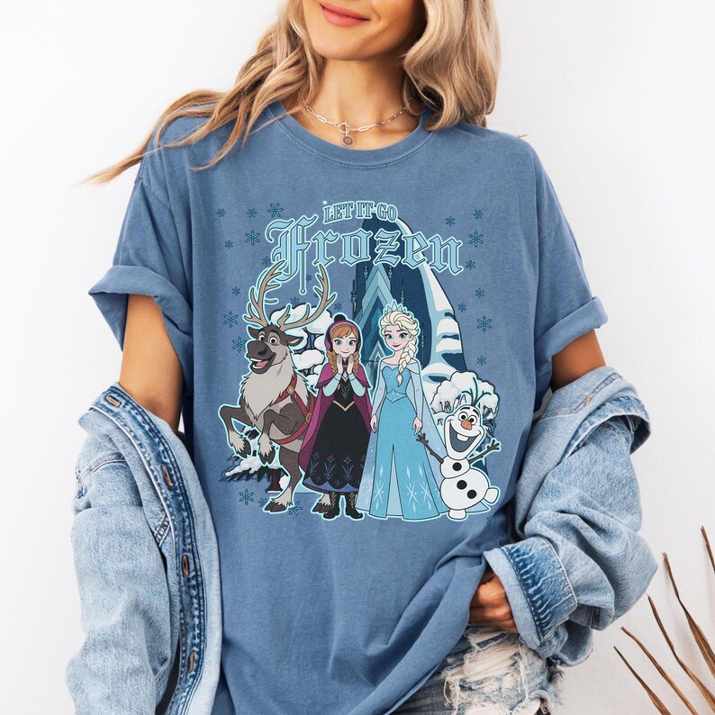 May include: Blue t-shirt featuring the text "Let It Go Frozen" with a graphic of characters from the movie Frozen, including Elsa, Anna, Olaf, and Sven. The design is set against a snowy mountain backdrop.
