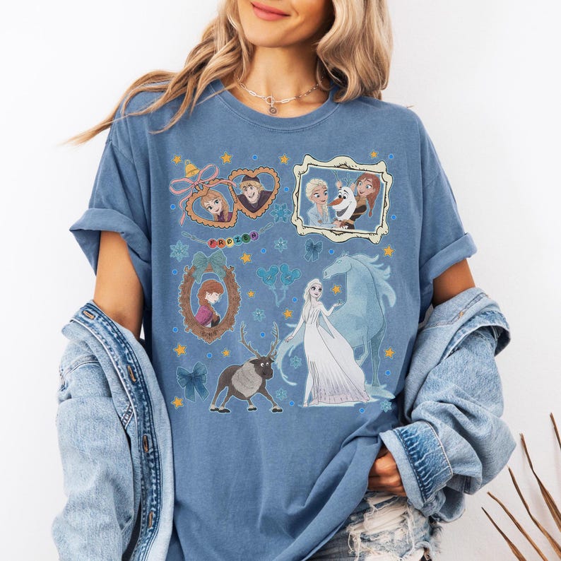Puede incluir: Camiseta azul con un dise&ntilde;o de personajes de la pel&iacute;cula "Frozen". El dise&ntilde;o incluye retratos enmarcados de Anna, Elsa, Olaf, Kristoff y Sven, con la palabra "Frozen". La camiseta tiene las mangas enrolladas.