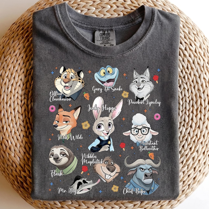 May include: A charcoal gray t-shirt featuring a graphic print of various animated animal characters. The characters include a cheetah, snake, lynx, fox, rabbit, sheep, sloth, beaver, and buffalo, each with their name printed in white script.