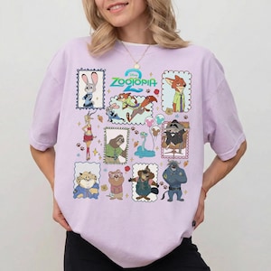May include: A light purple short-sleeve t-shirt featuring a colorful graphic print of various Zootopia characters in individual frames, including Judy Hopps, Nick Wilde, Flash, and others, with the Zootopia 2 logo centered at the top of the design.
