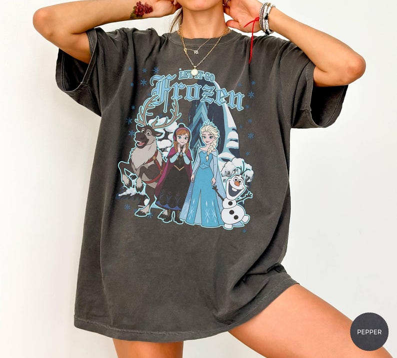 May include: Dark gray t-shirt featuring the text "Let Go Frozen" in blue, with a graphic of characters from the movie Frozen. The graphic includes Elsa, Anna, Olaf, and Sven. The shirt has short sleeves and a relaxed fit.