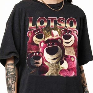 May include: Black t-shirt featuring a graphic of Lotso, the pink bear from Toy Story, with the word "LOTSO" in a gold and red font. The bear graphic has a variety of expressions.