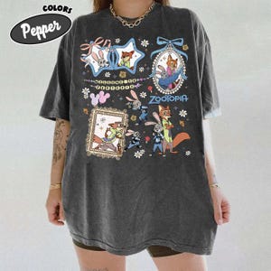 May include: A charcoal gray oversized t-shirt featuring a graphic print of Zootopia characters including Judy Hopps and Nick Wilde. The design includes multiple framed illustrations, floral accents, and the text Welcome to Zootopia and Zootopia.