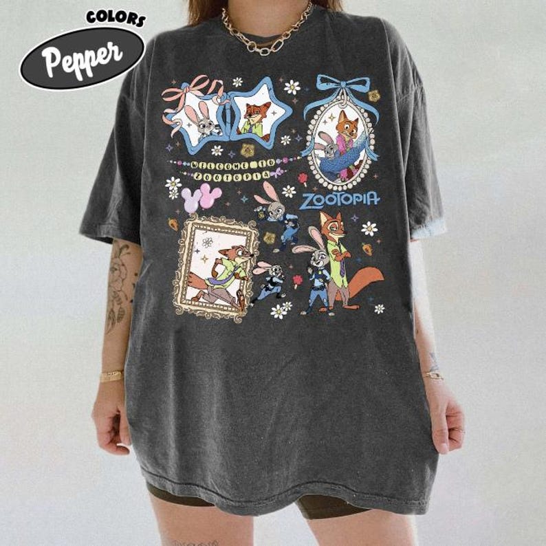 May include: A charcoal gray oversized t-shirt featuring a graphic print of Zootopia characters including Judy Hopps and Nick Wilde. The design includes multiple framed illustrations, floral accents, and the text Welcome to Zootopia and Zootopia.