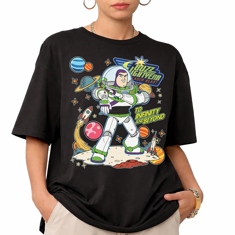 May include: Black t-shirt featuring a colorful graphic of Buzz Lightyear from Toy Story. The design includes the text "Buzz Lightyear Laser Blast" and "To Infinity and Beyond" with planets, rockets, and stars.