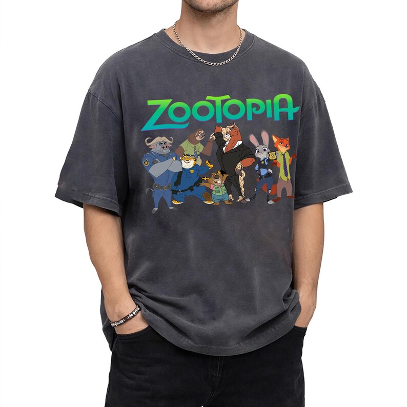 K&ouml;nnte beinhalten: Dunkelgraues T-Shirt mit dem Wort "Zootopia" in Gr&uuml;n und Blau sowie einer Grafik von Charakteren aus dem Animationsfilm. Das Shirt hat eine Vintage-Waschung und einen Rundhalsausschnitt.