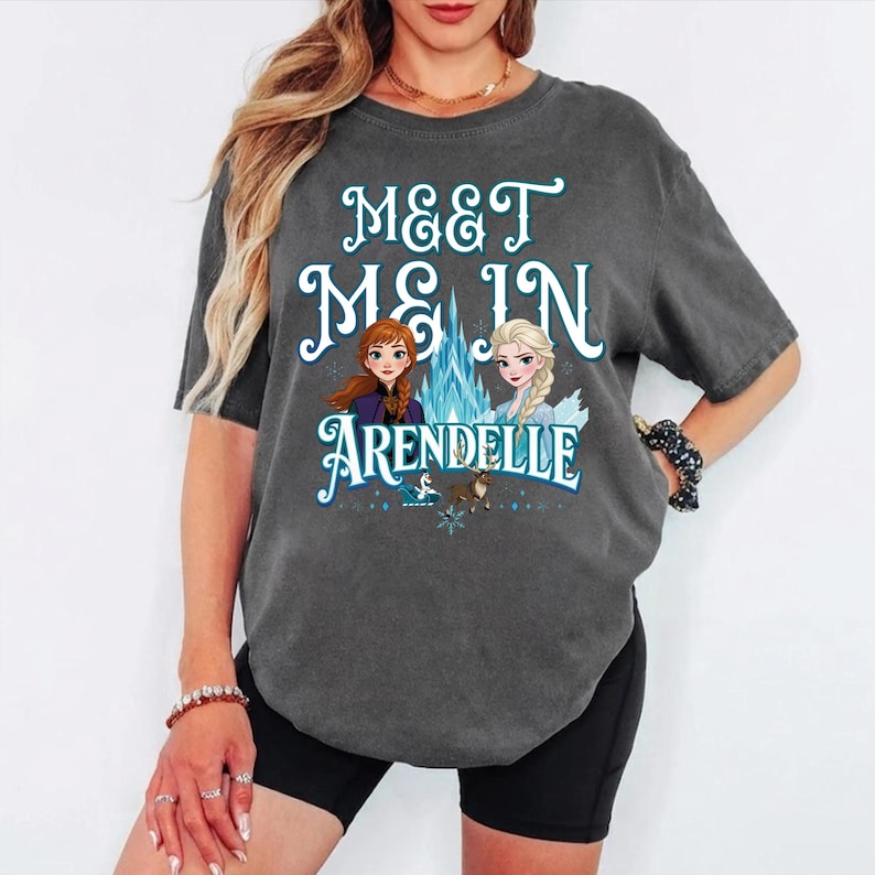 May include: Dark gray t-shirt with the text "MEET ME IN ARENDELLE" in white and teal lettering. The shirt features illustrations of two animated characters and a blue ice castle.