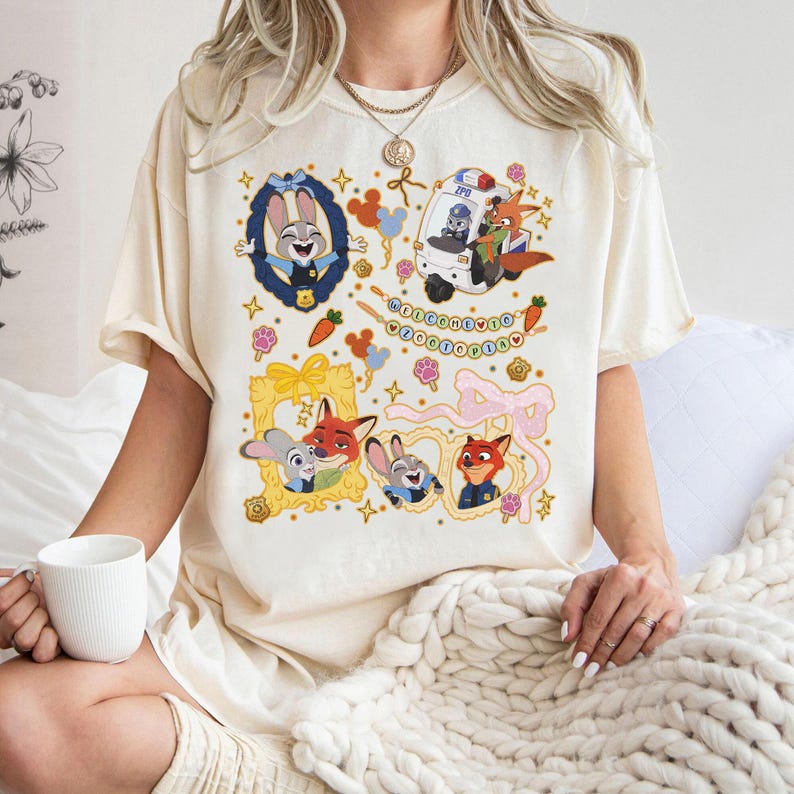 May include: Cream-colored t-shirt featuring cartoon characters from Zootopia. The design includes framed portraits of Judy Hopps and Nick Wilde, a police car, and the text "Welcome to Zootopia". Decorative elements include carrots, paw prints, and bows.