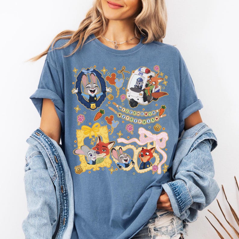 May include: Blue t-shirt featuring cartoon characters from Zootopia. The design includes Judy Hopps, Nick Wilde, and other characters in frames and a police vehicle. The text "WELCOME TO ZOOOTOPIA" is also present.