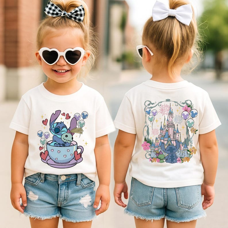 May include: A white short-sleeve t-shirt featuring a graphic of Stitch sitting in a teacup on the front and a detailed illustration of a castle with Stitch and fireworks on the back. The shirt is paired with light blue denim shorts.