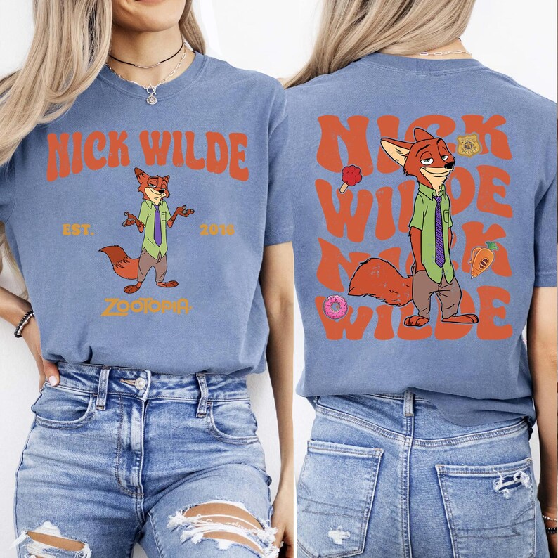 Pode incluir: Uma t-shirt azul com um gr&aacute;fico da personagem Nick Wilde de Zootopia. A frente apresenta o texto NICK WILDE EST. 2016 ZOOTOPIA. As costas mostram um gr&aacute;fico maior de Nick Wilde com o texto repetido NICK WILDE em cor de laranja.