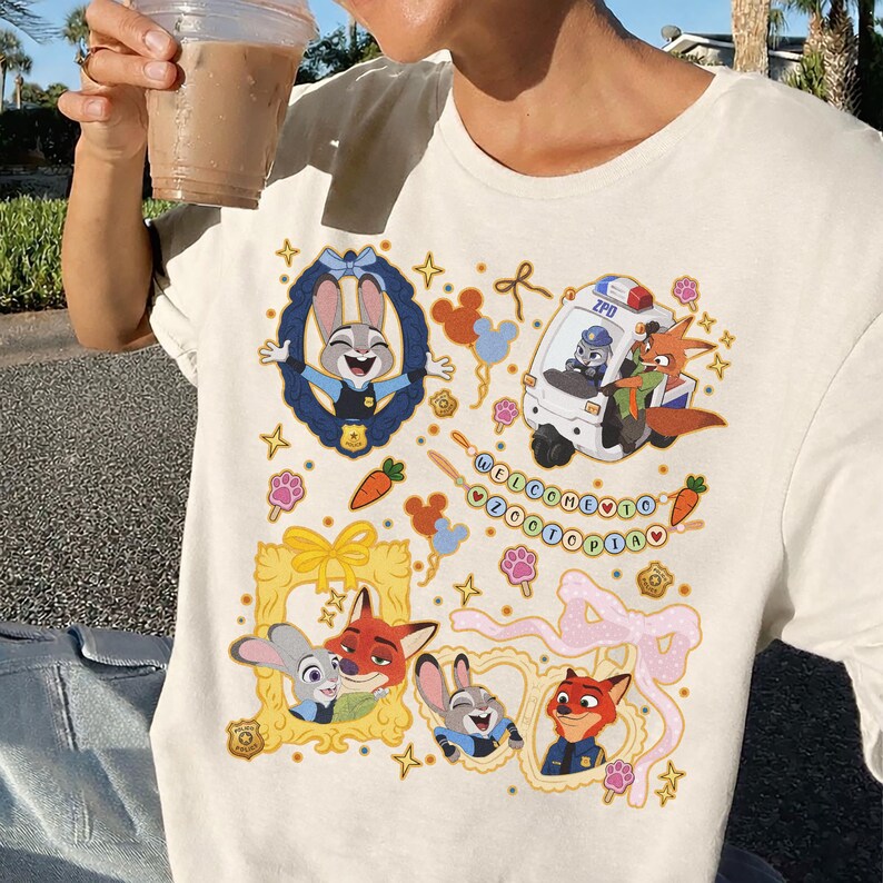 May include: Cream-colored t-shirt featuring colorful cartoon illustrations of characters from Zootopia. The design includes Judy Hopps, Nick Wilde, and a ZPD vehicle, with the text "WELCOME TO ZOOTOPIA".