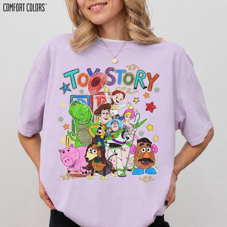 Może przedstawiać: Jasnofioletowa koszulka Comfort Colors z kolorową grafiką z Toy Story. Projekt zawiera napis "Toy Story" w zabawnej czcionce, a także wizerunki Chudego, Buzz'a Astrala i innych postaci z filmu.