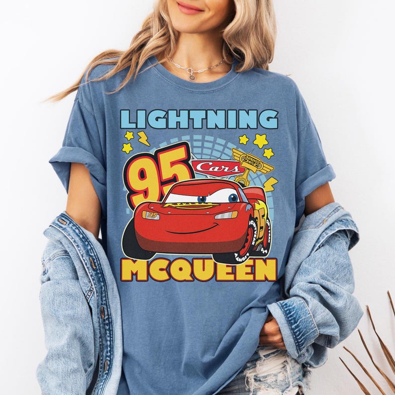 May include: Blue t-shirt featuring a graphic of Lightning McQueen from the Cars movie. The design includes the number 95, stars, and the text "Lightning McQueen" and "Cars". The shirt has rolled-up sleeves.