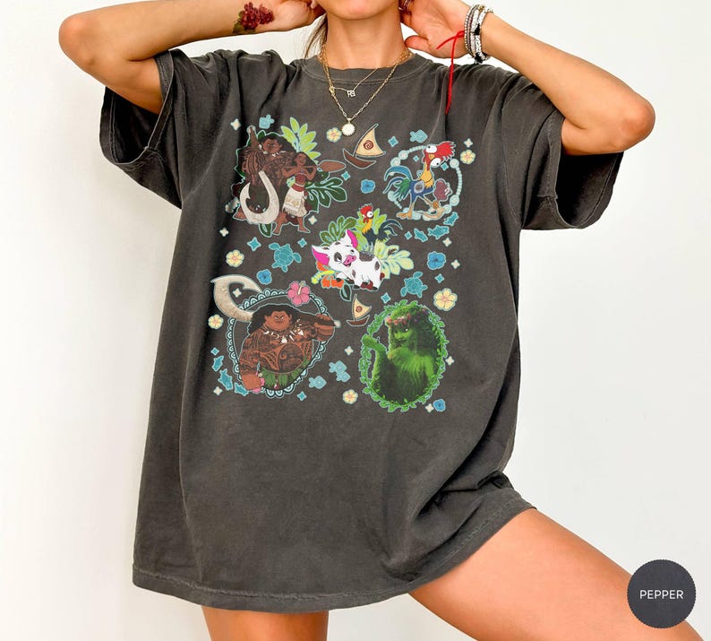 May include: Dark gray t-shirt featuring colorful cartoon characters in a square pattern. The design includes images of a rooster, a pig, and other characters. The shirt has short sleeves and a relaxed fit.