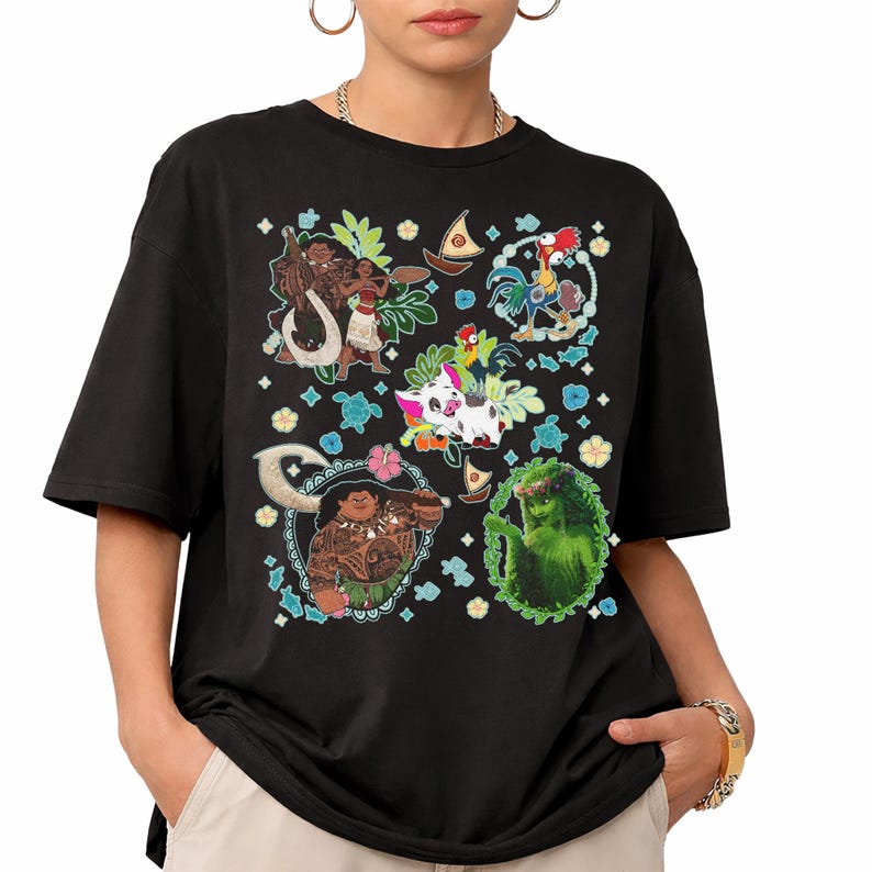 May include: Black t-shirt featuring colorful cartoon characters from the animated movie Moana. The design includes images of Maui, Moana, Hei Hei, Pua, and other tropical elements. The shirt is made of a soft material.