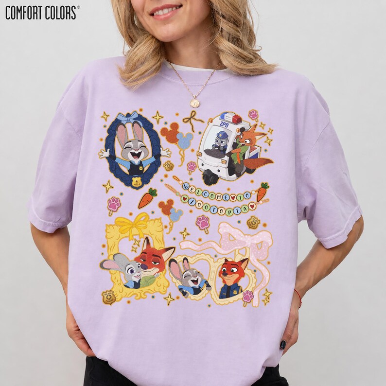 May include: A light purple Comfort Colors t-shirt featuring cartoon characters from Zootopia. The design includes Judy Hopps, Nick Wilde, and other characters in frames, a police vehicle, and the text "WELCOME TO ZOOOTOPIA".