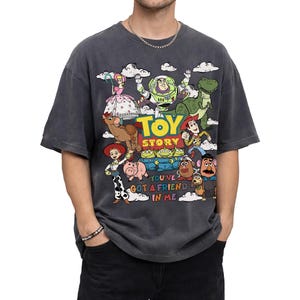 Op de afbeelding: Donkergrijs T-shirt met een kleurrijke afbeelding van personages uit de animatiefilm "Toy Story". Het ontwerp bevat Woody, Buzz Lightyear en andere personages, met de woorden "Toy Story" en "You've Got a Friend in Me".