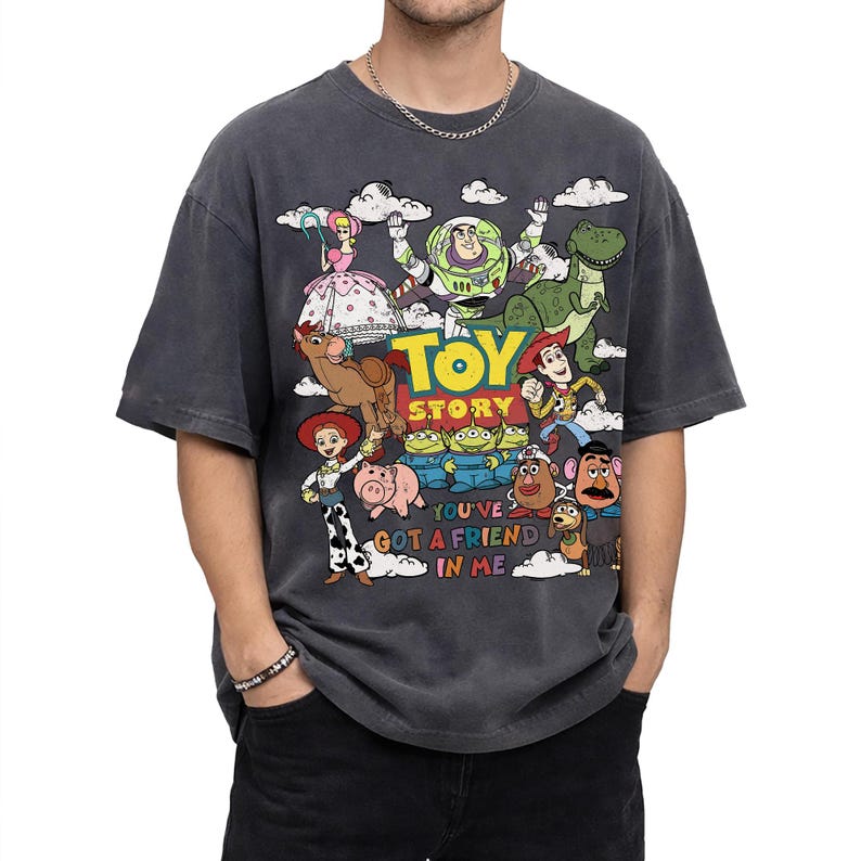 Op de afbeelding: Donkergrijs T-shirt met een kleurrijke afbeelding van personages uit de animatiefilm "Toy Story". Het ontwerp bevat Woody, Buzz Lightyear en andere personages, met de woorden "Toy Story" en "You've Got a Friend in Me".
