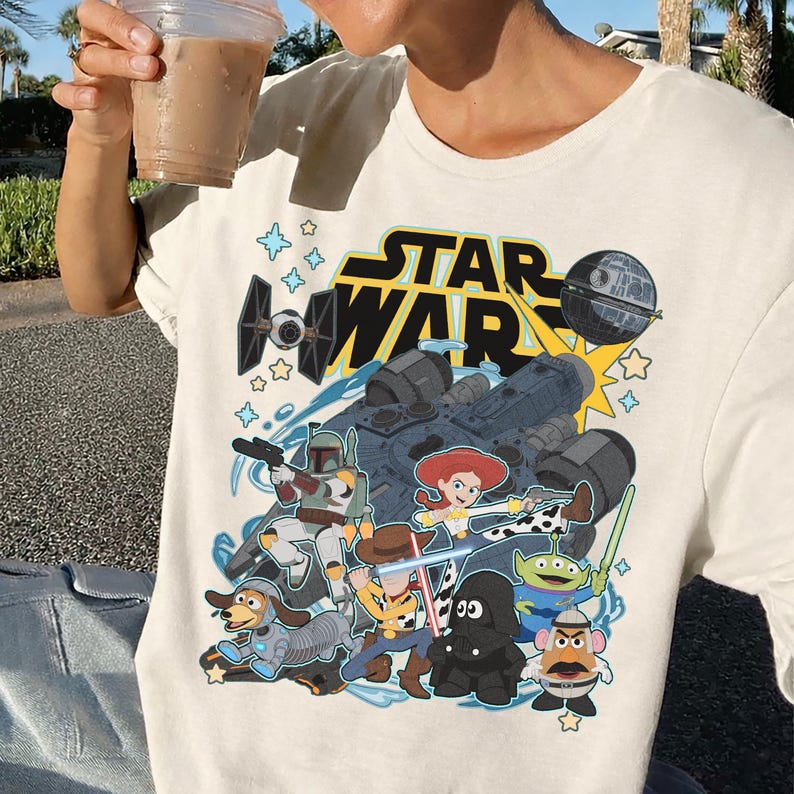May include: Cream-colored t-shirt featuring a graphic of Star Wars characters and the text "STAR WAR". The design includes a spaceship, the Death Star, and characters like Boba Fett, Woody, and Jessie.