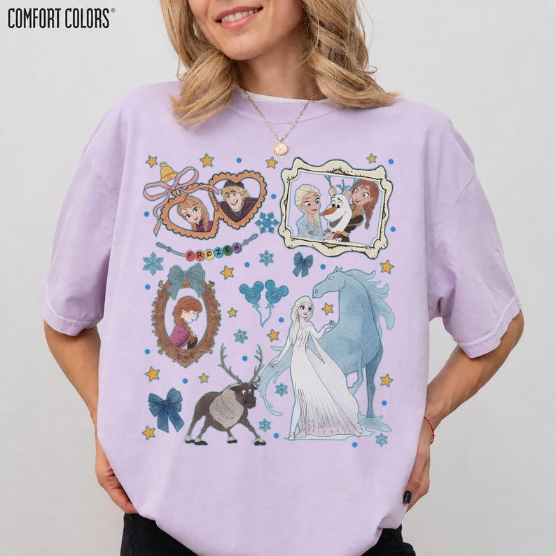 Puede incluir: Una camiseta Comfort Colors de color lila claro con ilustraciones de personajes de la pel&iacute;cula Frozen. El dise&ntilde;o incluye retratos enmarcados, copos de nieve, estrellas y la palabra "FROZEN".