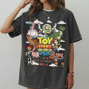 Op de afbeelding: Donkergrijze t-shirt met een kleurrijke afbeelding van personages uit de film "Toy Story". Het ontwerp bevat Woody, Buzz Lightyear en andere personages, met de tekst "Toy Story" en "You've Got a Friend in Me."