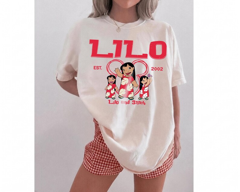 Puede incluir: Una camiseta de manga corta color hueso con un estampado gr&aacute;fico rojo. El texto dice LILO en la parte superior, EST. 2002 en el medio y Lilo and Stitch en la parte inferior. El gr&aacute;fico muestra tres personajes de Lilo con vestidos rojos florales.