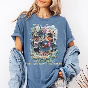 May include: Blue t-shirt featuring a colorful graphic of animated animal characters. The shirt has the text "we're wild and we can't be tamed" in a rainbow font. The shirt is a relaxed fit.