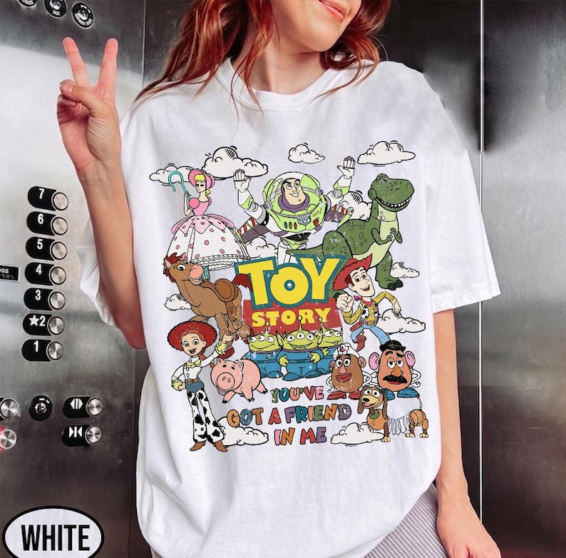 Op de afbeelding: Wit T-shirt met een kleurrijke afbeelding van personages uit de film "Toy Story". Het ontwerp bevat Buzz Lightyear, Woody en andere personages, met de tekst "TOY STORY" en "YOU'VE GOT A FRIEND IN ME."