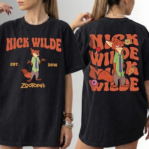 Pode incluir: Uma t-shirt preta com um gr&aacute;fico da personagem Nick Wilde de Zootopia. A frente apresenta o texto NICK WILDE EST. 2016 ZOOTOPIA. As costas mostram uma ilustra&ccedil;&atilde;o maior da personagem com o texto repetido NICK WILDE.