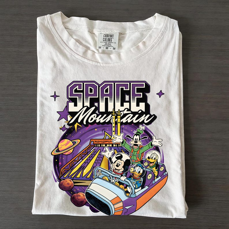 May include: White t-shirt with a graphic of Mickey Mouse, Donald Duck, and Goofy on a Space Mountain roller coaster. The design includes the words "SPACE MOUNTAIN" in purple and white, with stars and planets.