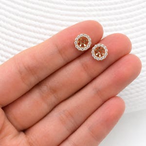 May include: Two circular gold earring jackets featuring a halo of small, clear, round-cut stones surrounding a central open setting. These jewellery components are designed to be worn behind a stud earring to add a decorative border of sparkle.