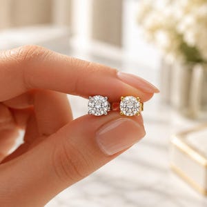 May include: Two round-cut stud earrings featuring clear, faceted stones held in four-prong settings. One earring is set in a silver-toned metal, while the other is set in a gold-toned metal, both displaying a brilliant, reflective surface.