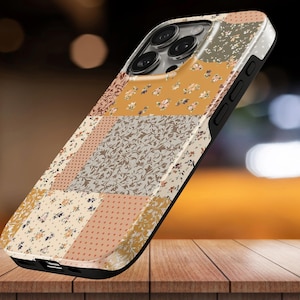 Op de afbeelding: Een smartphonehoesje met een patchworkontwerp van diverse patronen, waaronder bloemenprints, stippen en bladranken in tinten mosterdgeel, crème, beige en bruin. Het hoesje heeft een zwart frame en een uitsparing voor de cameralens.