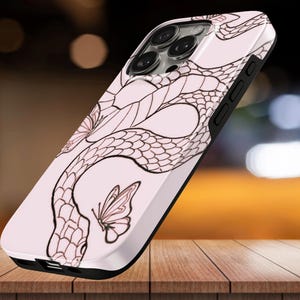 Puede incluir: Una funda para smartphone de color rosa claro con una ilustración de líneas de color marrón oscuro que muestra una serpiente sinuosa y una mariposa. La funda tiene un borde negro y un recorte para las lentes de la cámara en la parte trasera.