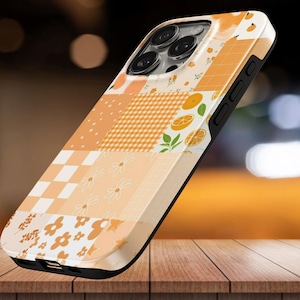 Puede incluir: Una funda para smartphone con un diseño de patchwork en tonos naranja, crema y blanco. El patrón incluye rodajas de naranja, hojas verdes, cuadrados a cuadros e ilustraciones de flores sencillas en la parte trasera y los laterales.