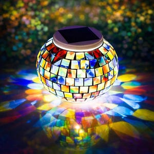 May include: A spherical solar-powered mosaic glass lantern. The lantern is composed of colorful, irregularly shaped glass tiles in shades of red, yellow, blue, and green. The lantern's top features a dark square solar panel. The light casts colorful shadows.