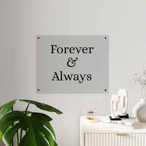 May include: A rectangular light gray wall sign featuring the black text Forever & Always centered on the surface. The sign is mounted with four small circular silver-toned hardware fasteners, one located at each of the four corners of the plaque.