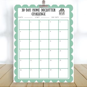 Könnte beinhalten: Ein druckbarer 30-Tage-Home-Declutter-Challenge-Kalender. Der Kalender hat einen mintgrünen Rand mit einem gewellten Rand und eine Kopfzeile mit der Aufschrift "30-DAY HOME DECLUTTER CHALLENGE". Der Kalender ist auf einer Holzoberfläche befestigt.