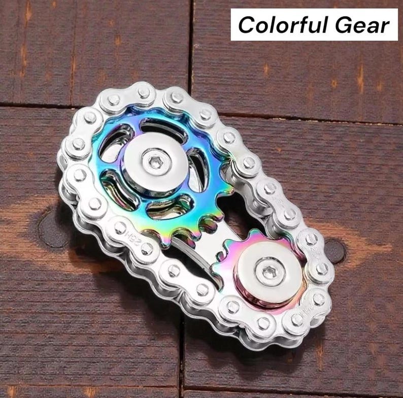 May include: A silver metal fidget spinner in the shape of a bicycle chain and gears. The center gear has a rainbow iridescent finish. The text "Colorful Gear" is in a white rectangle in the top right corner.