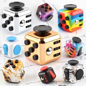 Pode incluir: Uma coleção de nove cubos de inquietação com vários acabamentos e padrões, incluindo designs em prata metálica, ouro, arco-íris, galáxia, camuflagem e salpicos de tinta. Cada cubo apresenta elementos táteis como botões, interruptores e rolos.