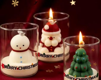 Puede incluir: Tres velas navideñas encendidas en portavelas de vidrio. Una es un muñeco de nieve, otra es Papá Noel y la otra es un árbol de Navidad. Cada vela tiene una base blanca con la inscripción "MERRY CHRISTMAS". El fondo es rojo oscuro.
